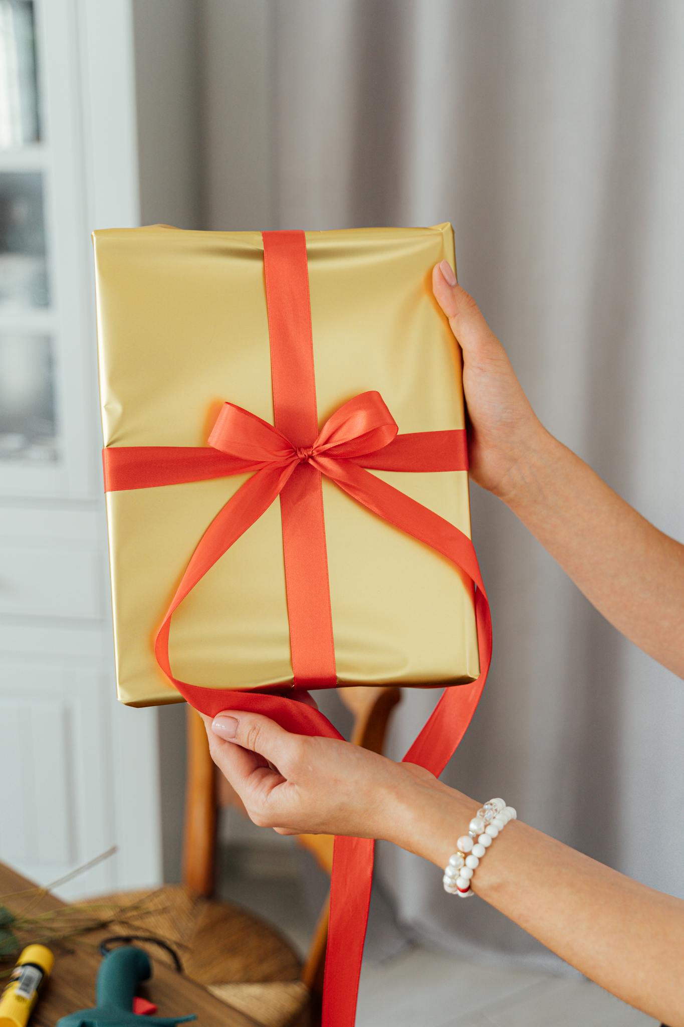 A beautifully wrapped gold gift with red ribbon held by hands, perfect for celebrations.