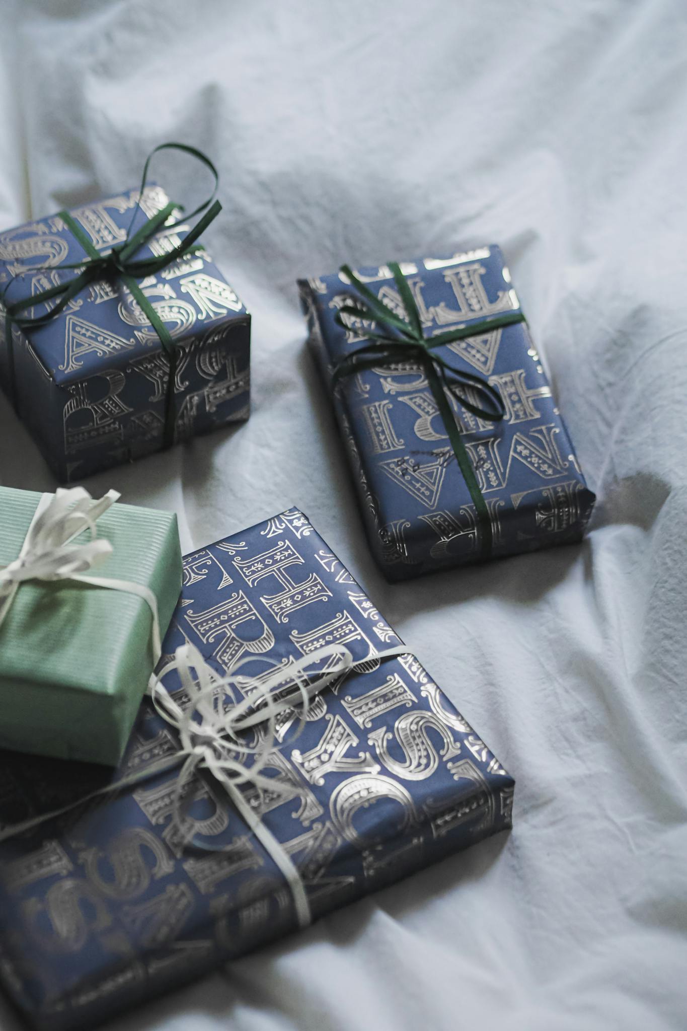 Beautifully wrapped gifts with blue and green paper elegantly arranged on soft white fabric.
