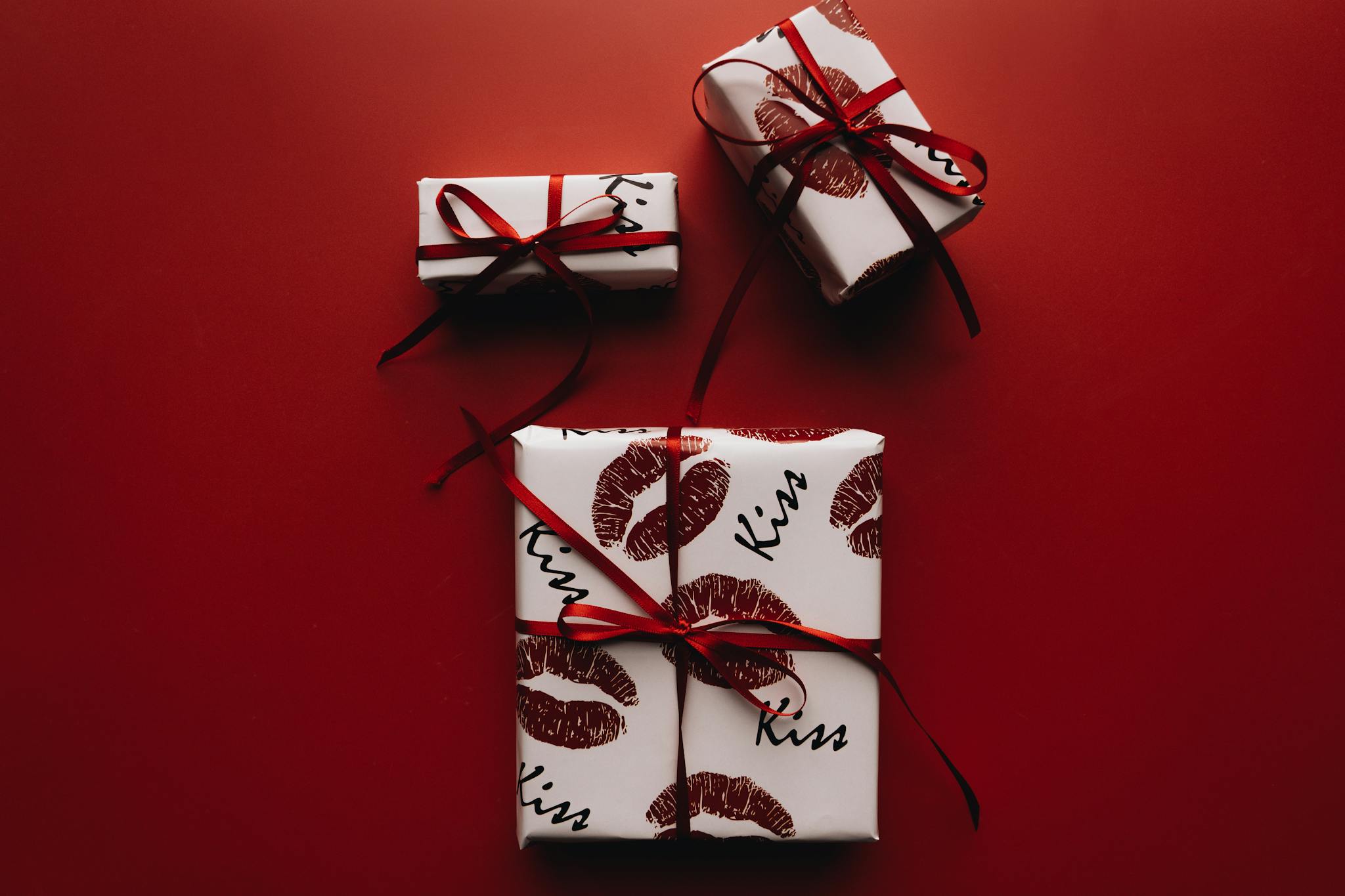 Stylish gift boxes wrapped with lip-print paper and red ribbons on a red background.